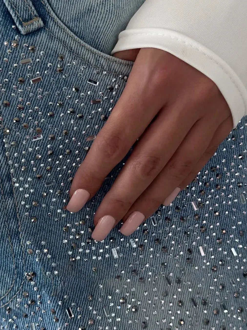 Main féminine sur veste en jean ornée de strass, manucure nude élégante