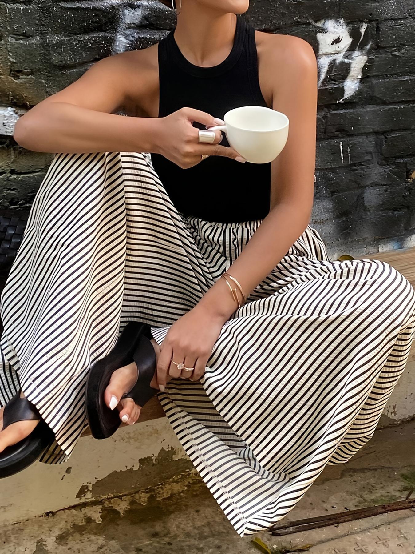 Femme en tenue mode féminine avec jupe rayée et top noir, tenant une tasse