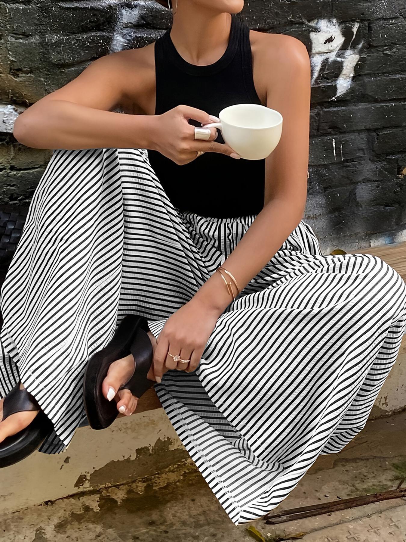 Femme en tenue mode féminine avec pantalon rayé noir et blanc, top noir et sandales, tenant une tasse